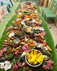 a long table filled with lots of food on top of a green cloth covered table