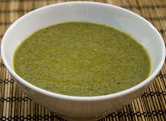 a white bowl filled with green soup sitting on top of a bamboo place mat next to a spoon