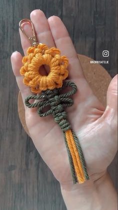 a hand holding a yellow and green crochet keychain with a flower on it