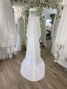 wedding gowns and dresses on display in a bridal room with white flowers hanging from the ceiling