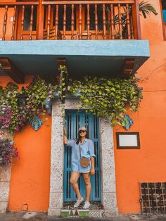 a woman standing in the doorway of an orange and blue building with plants growing on it