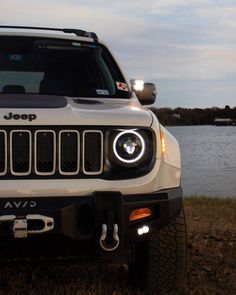 the front end of a white jeep parked next to a body of water