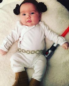 a baby laying on top of a white rug wearing a star wars outfit and holding a remote control