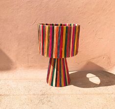 a multicolored striped lamp shade sitting on the side of a pink stucco wall