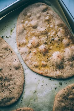 three pita breads sitting on top of a baking pan covered in seasoning