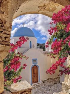 an arched doorway with pink flowers growing on it and a blue dome in the background