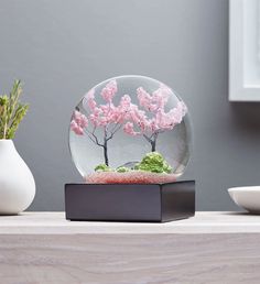 a snow globe with pink flowers in it on a table next to two vases