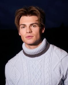 a young man wearing a white sweater looks into the camera