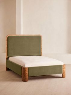 a bed with a wooden frame and green upholstered headboard, in an empty room