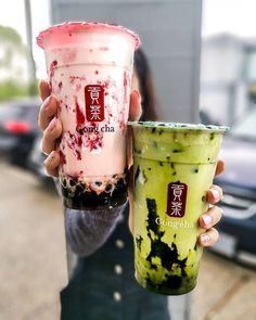 a person holding up a drink in front of a building with chinese writing on it