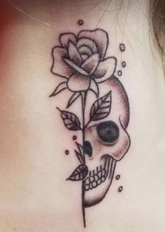 a woman's neck with a skull and rose tattoo on it