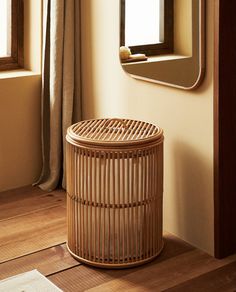 a bamboo basket sitting on the floor in front of a window with curtains behind it