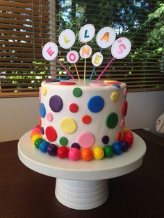 a birthday cake decorated with polka dots and nameplates on a table in front of a window