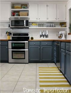 a kitchen with gray cabinets and white walls, yellow rugs on the floor in front of the stove