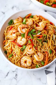 two bowls filled with noodles and shrimp on top of a marble countertop next to silver utensils