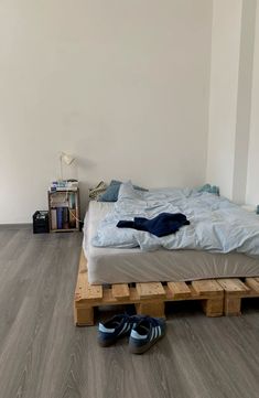 a bed made out of wooden pallets with shoes on the floor next to it