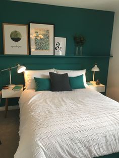 a bedroom with green walls and white bedspread, two framed pictures on the wall