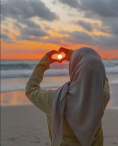 a woman wearing a headscarf looking at the sun through her heart shaped sunglasses