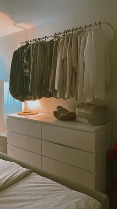 a white bed sitting next to a dresser with clothes hanging on it