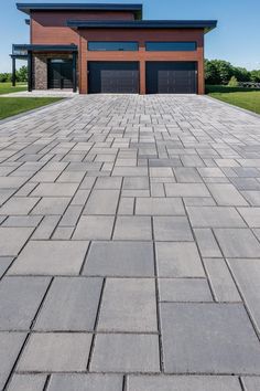 a large brick driveway with two garages in the background and grass on both sides