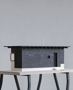 a table with a birdhouse on top of it next to a gray wall and black legs