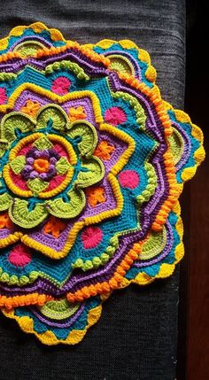 a colorful crocheted doily is displayed on a black cloth with wood background