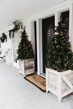 two christmas trees are placed in wooden crates on the front porch, decorated with greenery