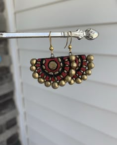 a pair of earrings hanging from a hook on a house door hanger with gold and red beads