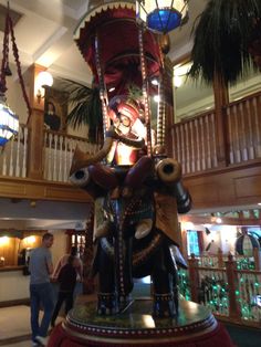 an elephant statue in the middle of a lobby with people standing around it and lights hanging from the ceiling