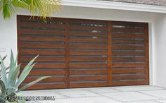 an image of a garage door that is made out of wood and has plants in the foreground