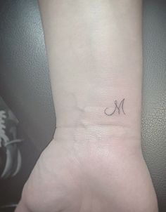 a small wrist tattoo with the letter m on it