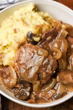 a white bowl filled with meat, potatoes and gravy on top of a wooden table