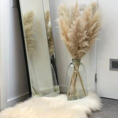 a vase filled with dry grass next to a tall mirror on the floor in front of a door