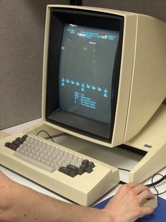 a man is typing on a computer with an old style keyboard and monitor in front of him