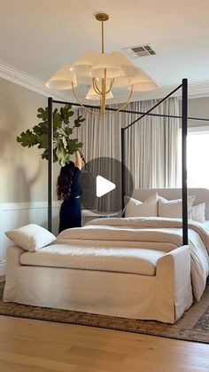 a woman standing in front of a four poster bed with white linens and pillows