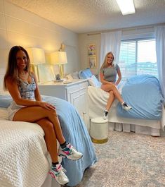 two women sitting on beds in a bedroom with blue sheets and white beddings