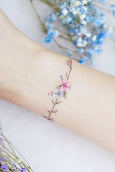 a woman's arm with flowers on it and the wrist is covered in tattoos