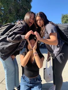 three girls standing together making a heart with their hands