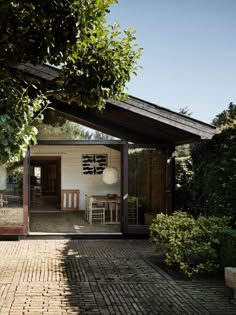 a small white house sitting next to a lush green tree on top of a brick walkway