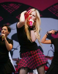 two women singing on stage with one holding a microphone and the other wearing a skirt