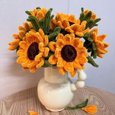 a white vase filled with yellow flowers on top of a wooden table