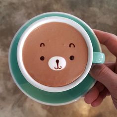 a hand holding a cup of hot chocolate with a bear face on it