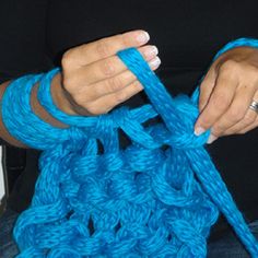 a woman is holding a blue crochet piece in her hands and knitting it