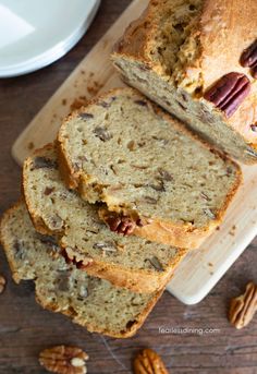 sliced loaf of pecan nut bread on top of a cutting board next to some pecans