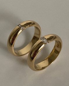 two gold wedding rings with diamond stones on each one, sitting next to each other