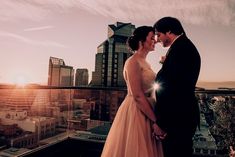 a bride and groom standing on top of a building with the sun setting behind them