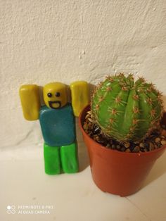 a lego man standing next to a cactus in a clay pot on a white surface