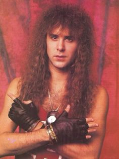 a man with long hair and leather gloves posing for a photo in front of a red background