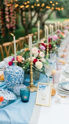 the table is set with blue and white dishes, candles, and flowers in vases