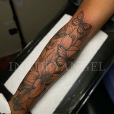 a woman's arm with flowers and butterflies tattoo on her left forearm, in black and white